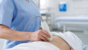 Soignante réalisant un bladder scan sur le bas-ventre d’un patient dans une chambre d’hôpital moderne.