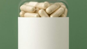 Pot transparent rempli de gélules avec une étiquette blanche vierge sur fond vert